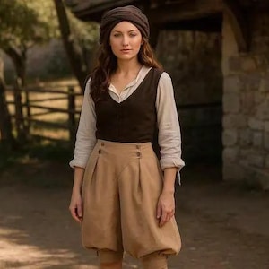 May include: A woman wearing a brown turban, a white blouse, a dark brown vest, and tan, high-waisted, pleated breeches. The outfit has a historical or rustic aesthetic. The background includes trees, a wooden fence, and a stone building.