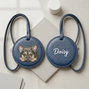May include: Two round navy blue luggage tags with matching straps. One tag features a detailed illustration of a French Bulldog with brown and black fur. The other tag displays the name Daisy in white cursive script lettering on the textured surface.