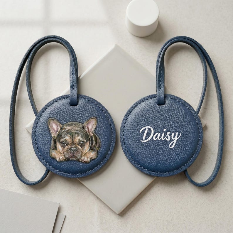 May include: Two round navy blue luggage tags with matching straps. One tag features a detailed illustration of a French Bulldog with brown and black fur. The other tag displays the name Daisy in white cursive script lettering on the textured surface.