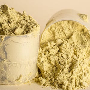 Pu&ograve; includere: Due misurini di plastica trasparente riempiti con una polvere verde chiaro. Un misurino &egrave; in posizione verticale e trabocca, mentre l'altro &egrave; rovesciato, versando la polvere. La polvere sembra essere un integratore o un additivo alimentare.