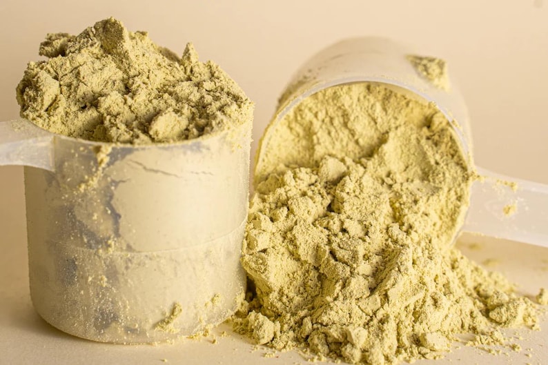 Pu&ograve; includere: Due misurini di plastica trasparente riempiti con una polvere verde chiaro. Un misurino &egrave; in posizione verticale e trabocca, mentre l'altro &egrave; rovesciato, versando la polvere. La polvere sembra essere un integratore o un additivo alimentare.