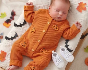 May include: An orange baby jumpsuit with pumpkin appliqués and buttons, paired with white sneakers. The baby is lying on a white, textured surface decorated with Halloween-themed cutouts of bats and leaves. A cozy and festive outfit.