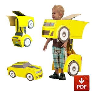 Puede incluir: Un niño lleva un disfraz de coche de cartón amarillo con grandes ruedas blancas. El disfraz tiene forma de coche transformador. También se ve un coche de cartón separado y un icono de descarga PDF.