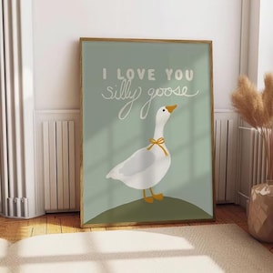 May include: A framed art print featuring a white goose with a yellow bow, standing on a green hill against a light green background. The text "I LOVE YOU silly goose" is written in white script.