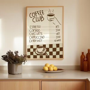 May include: A framed sign with the words "COFFEE CLUB" in a handwritten style. The sign lists coffee drinks with options like "ICED" and "ALWAYS." A checkered pattern is at the bottom. The sign is above a countertop with lemons and a vase.
