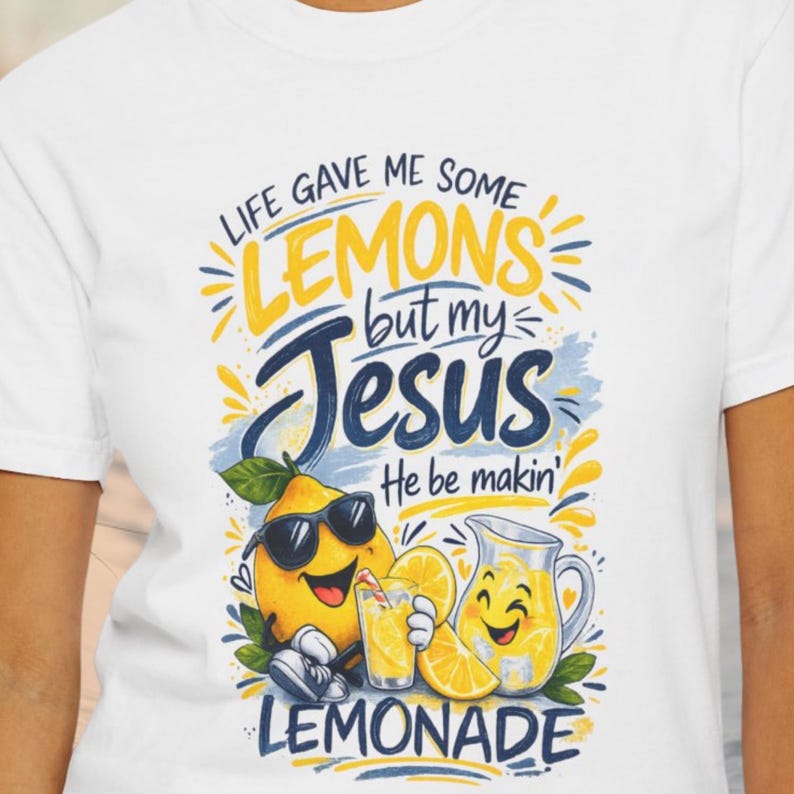 Christian lemon graphic shirt with the phrase “Life Gave Me Some Lemons But My Jesus He Be Makin’ Lemonade” featuring cute lemon characters and lemonade pitcher on white t-shirt.