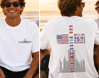 May include: A white t-shirt featuring a small graphic on the front chest with the text WE WILL NEVER FORGET GOD BLESS AMERICA. The back displays a large graphic with an American flag, the text GOD BLESS AMERICA, and SEPT 11, 2001 25TH ANNIVERSARY.