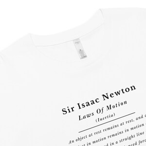 May include: White t-shirt featuring the text "Sir Isaac Newton Laws Of Motion (Inertia)". The shirt has a classic crew neck and a tag near the collar. The text is in a simple, readable font.