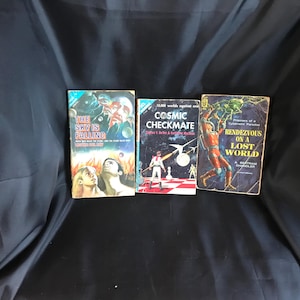 May include: Three vintage science fiction paperback books with colorful covers. Titles include "The Sky is Falling," "Cosmic Checkmate," and "Rendezvous on a Lost World." The books are arranged on a dark background.