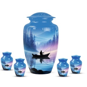 May include: A set of blue cremation urns with a serene landscape design. The main urn features a fisherman in a boat on a lake, surrounded by mountains and trees. Smaller urns echo the design. A peaceful and reflective memorial.