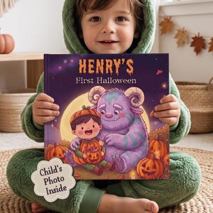 Op de afbeelding: Een hardcover boek getiteld Henry's First Halloween met een paarse kaft waarop een kind en een paars monster tussen oranje pompoenen onder een volle maan staan. Een witte sticker op de kaft bevat de tekst Child's Photo Inside.