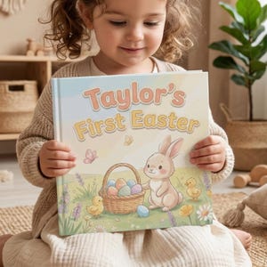 May include: A child holding a book titled "Taylor's First Easter". The cover illustration shows a cartoon bunny, a basket of Easter eggs, and two chicks in a field with butterflies. The title is in peach and yellow.