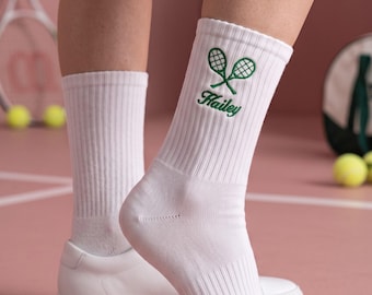 Puede incluir: Un par de calcetines blancos de canalé con un diseño bordado de dos raquetas de tenis verdes cruzadas sobre el nombre Hailey en cursiva verde. Los calcetines están hechos de una tela suave y llegan hasta la mitad de la pantorrilla.