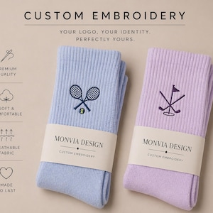 Puede incluir: Dos pares de calcetines acanalados en azul claro y lavanda, cada uno con bordado personalizado. El par azul muestra raquetas de tenis cruzadas y una pelota, el par lavanda palos de golf cruzados y una bandera. Ambos tienen etiquetas Monvia Design.