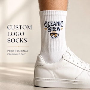 May include: White ribbed crew socks featuring the embroidered text Oceanic Brew in dark blue with a gold and blue coffee cup graphic. The socks are worn with white leather sneakers. Text on the left reads Custom Logo Socks Professional Embroidery.