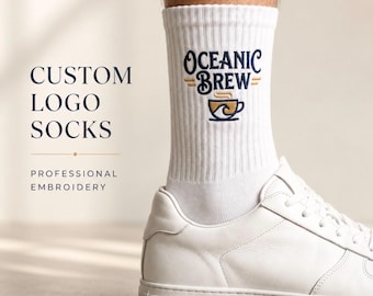 Puede incluir: Calcetines blancos de canalé con el texto bordado Oceanic Brew en azul oscuro y un gráfico de una taza de café en dorado y azul. Los calcetines se llevan con zapatillas blancas. El texto a la izquierda dice Custom Logo Socks Professional Embroidery.