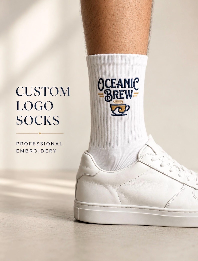 Puede incluir: Calcetines blancos de canal&eacute; con el texto bordado Oceanic Brew en azul oscuro y un gr&aacute;fico de una taza de caf&eacute; en dorado y azul. Los calcetines se llevan con zapatillas blancas. El texto a la izquierda dice Custom Logo Socks Professional Embroidery.