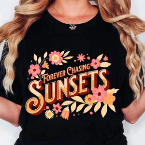 May include: Black t-shirt with the text "Forever Chasing Sunsets" in a retro font, adorned with pink and yellow floral accents. The design features a vintage aesthetic, perfect for casual wear.
