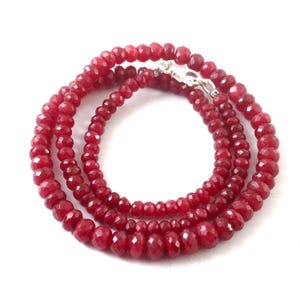 May include: A layered necklace composed of faceted, deep red gemstones. The beads vary in size, creating a graduated effect. A silver-toned clasp secures the necklace. The jewelry is displayed against a white background.
