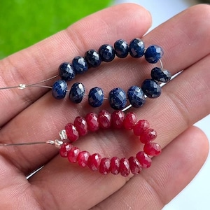 May include: Two strands of gemstone beads. One strand features faceted, dark blue beads, and the other has faceted, deep red beads. The beads are strung on thin, silver-colored wire, ready for jewelry making.