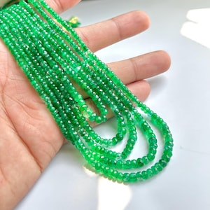 Puede incluir: Varias hebras de collares de piedras preciosas de color verde brillante. Los collares están hechos de pequeñas cuentas facetadas y se muestran en una mano. Las cuentas tienen un aspecto brillante y pulido, y el efecto general es de color y elegancia vibrantes.