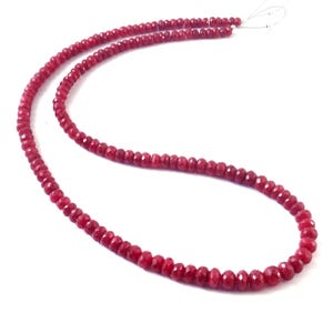 May include: A necklace of small, faceted, deep red beads. The beads are strung together, creating a continuous strand. The necklace is shown against a white background, emphasising the colour and texture of the beads.