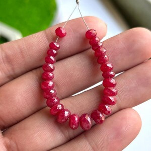May include: A string of faceted, deep red ruby beads. The beads are strung on a thin, silver-coloured wire, forming a teardrop shape. The gemstones have a brilliant, polished finish, reflecting light. The beads are small, suitable for jewellery making.