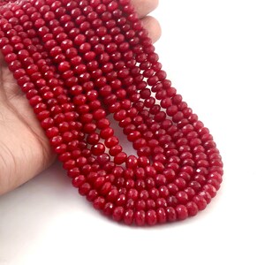 Può includere: Una collezione di perline rosse profonde e sfaccettate. Le perline sono infilate insieme, creando più fili. Le perline hanno dimensioni e forma costanti e il colore è uniforme. Lo sfondo è bianco.