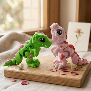 Peut inclure: Deux figurines de dinosaures articulées, l'une verte avec des cœurs roses et l'autre rose avec des cœurs rouges, sont posées sur une surface en bois. Les dinosaures ont de grands yeux noirs et se font face. Des pétales de fleurs séchées et une petite fleur sont éparpillés.