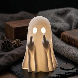 Può includere: Una statuetta di fantasma bianca stampata in 3D e illuminata dall'interno, con due occhi ovali e due braccia sollevate con i medi tesi. La superficie del fantasma presenta visibili linee di strato orizzontali dovute alla stampa 3D.