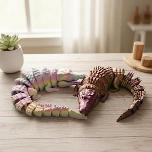 May include: Two articulated crocodile toys. One is a rainbow of pastel colours, the other is brown and purple. The toys are on a light wood surface. The crocodile toys are a fun and unique gift idea.