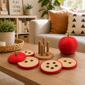 May include: A wooden stacking toy shaped like a red apple, consisting of a circular base with five vertical pegs and several flat, round, red and tan wooden discs with varying hole patterns that can be stacked onto the pegs to form the apple.