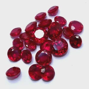 May include: A scattering of faceted, deep red rubies. The gemstones vary in size and shape, with a brilliant, reflective surface. The rubies are scattered against a white background, showcasing their rich colour and clarity. Suitable for jewellery making.