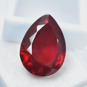 Può includere: Una gemma sfaccettata a forma di pera di colore rosso intenso e saturo. La pietra presenta una superficie lucida con molteplici sfaccettature geometriche che riflettono la luce, creando un aspetto brillante con varie tonalità di rosso scuro.
