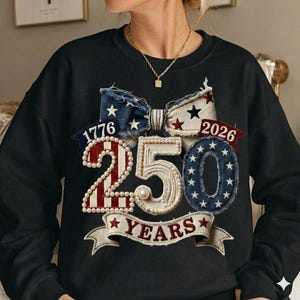 May include: Black sweatshirt with a patriotic design. Features a bow with stars and stripes, the numbers "1776" and "2026", and the number "250" with "YEARS" on a banner. The design incorporates red, white, and blue.