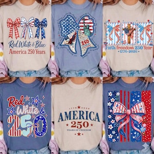 Puede incluir: Seis camisetas con diseños patrióticos en rojo, blanco y azul. Cada camiseta presenta gráficos como lazos, estrellas y el texto "America 250 Years" o frases similares. Las camisetas están sobre un fondo claro.