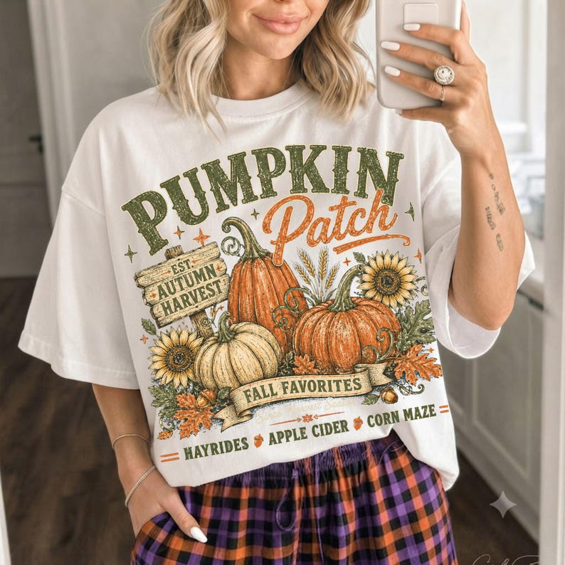 May include: A white t-shirt featuring a graphic print with the text PUMPKIN Patch, EST. AUTUMN HARVEST, FALL FAVORITES, HAYRIDES, APPLE CIDER, and CORN MAZE. The design includes orange pumpkins, yellow sunflowers, and autumn leaves.