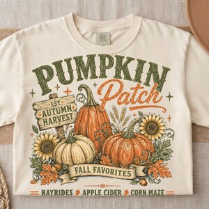 May include: A cream-colored t-shirt featuring a graphic with the text PUMPKIN Patch, EST. AUTUMN HARVEST, FALL FAVORITES, HAYRIDES, APPLE CIDER, and CORN MAZE. The design includes orange and white pumpkins, sunflowers, and autumn leaves.
