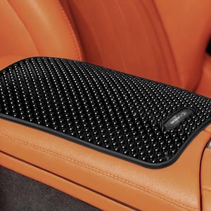 May include: Black textured car console cover with a small logo, set against an orange leather interior. The cover has a raised, dotted pattern and a black border. The car interior features a silver accent.