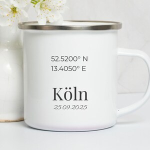 Könnte beinhalten: Weißer Emaille-Becher mit silbernem Rand, mit den Koordinaten 52.5200° N 13.4050° E, dem Wort "Köln" und dem Datum 25.09.2025 in Schwarz. Eine weiße Vase mit weißen Blumen im Hintergrund.