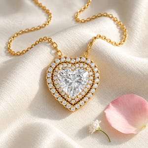 May include: A gold necklace featuring a heart-shaped pendant with a large central heart-cut clear stone, surrounded by two concentric rows of small round clear stones, suspended from a delicate gold chain link necklace.