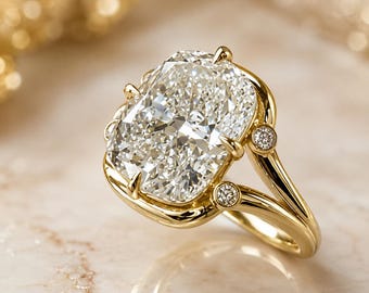 May include: A gold ring featuring a large, rectangular cushion-cut clear gemstone held by multiple prongs. The band splits into two sections, each accented with a small, round, clear gemstone set into the gold metal near the center stone.