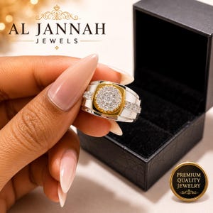 May include: A two-tone ring featuring a central circular cluster of small clear stones set in a gold-colored mount, flanked by silver-colored bands embedded with additional clear stones, presented with a black jewelry box and Al Jannah Jewels branding.