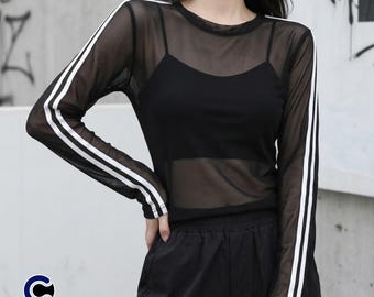May include: A black long-sleeve sheer mesh top featuring a round neckline and two parallel white stripes running down the length of each sleeve. The garment is worn over a solid black camisole and is paired with black pants. The logo CASUALWEAR BYPAOLO is visible.
