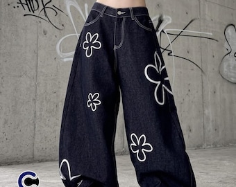 May include: Dark wash denim jeans with a wide leg design. The jeans feature white floral outlines and white stitching. The jeans have the text "CASUALWEAR" in a white font with a blue "C" logo.