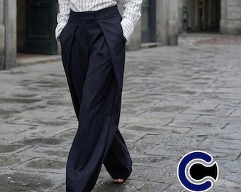 May include: Navy blue pinstripe trousers with a wide leg design. The trousers have a high waist and a wrap-style front. The model is wearing a white and light blue striped button-down shirt. The Casualwear by Paolo logo is in the bottom right corner.