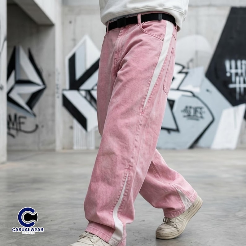 Peut inclure: Pantalon en jean rose clair avec une bande blanche sur le c&ocirc;t&eacute;. Le pantalon a une coupe ample et est port&eacute; avec une ceinture noire et des baskets blanches. L'arri&egrave;re-plan pr&eacute;sente du graffiti.