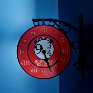 Peut inclure: Une horloge rouge et noire avec l'inscription "Platform 9 3/4 Hogwarts Express" sur un mur bleu. L'horloge a des chiffres romains et des aiguilles noires. L'horloge est fixée sur un support en métal noir.