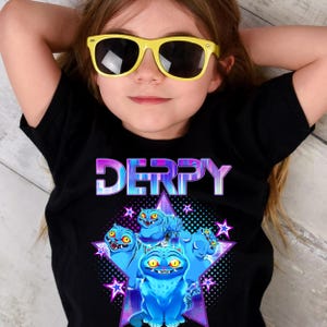 May include: Black t-shirt with the word "DERPY" in a pixelated font and a graphic of blue cartoon cats. The cats are arranged in a star shape with purple and blue accents. The person in the image is wearing yellow sunglasses.