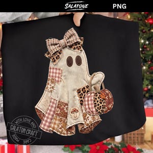 May include: A black t-shirt featuring a ghost graphic made of various brown and beige fabric patches. The ghost has a plaid bow, two dark oval eyes, and holds a small pumpkin. A mushroom patch is visible on the ghost's body. The text SALATONE is at the top.
